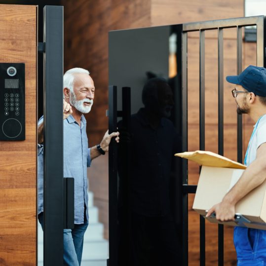 Happy senior man communicating with a courier who is delivering packages to his home.